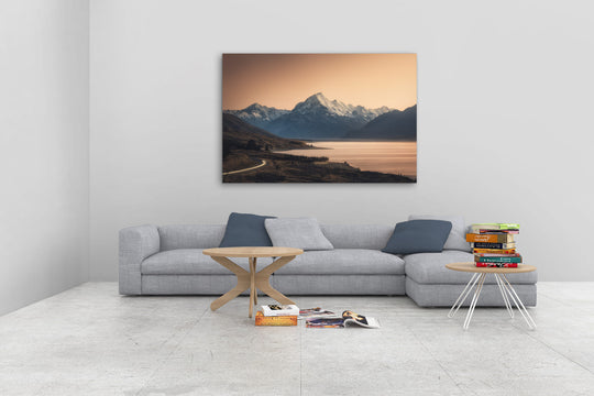 Mountain photo wall art in neutral lounge setting with a grey couch, coffee tables and books