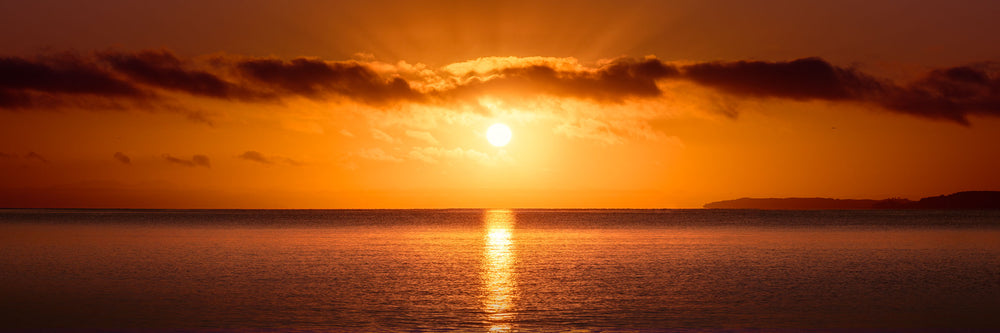 Bright orange sun rising up over the horizon at Hatfields Beach, reflected in the sea below.