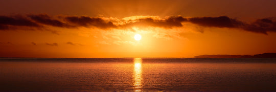 Bright orange sun rising up over the horizon at Hatfields Beach, reflected in the sea below.