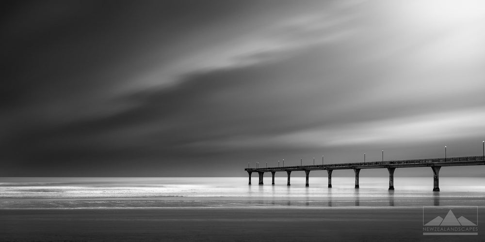 Black and white panorama photo of a pier over the sea with dark clouds above.