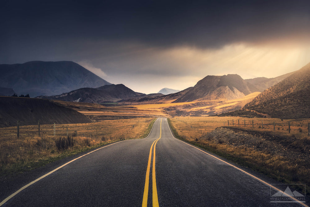 road in the centre of the photo leading towards mountains with dark moody clouds above.