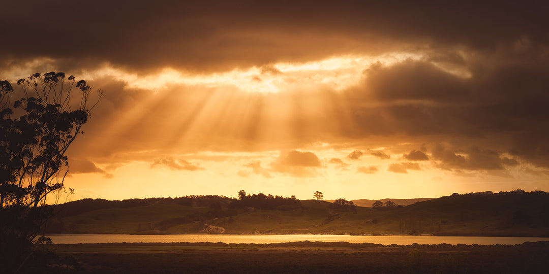 Panorama landscape of golden sunbeams through the clouds over hills and sea.