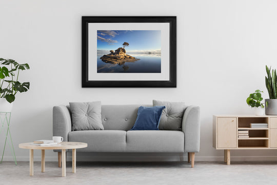 Framed photo wall art print of a New Zealand landscape with a grey couch, plants and table.