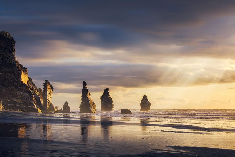 NZ landscape photo of the Three Sisters in Tongaporutu with rocks, sea and the sun setting behind the horizon