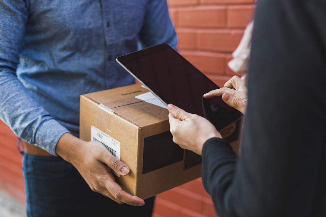 Image of a person receiving a boxed package and the delivery person holding an ipad.