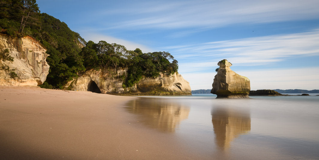 Panorama beach scene of Cathedral Cove reflected in the sand.