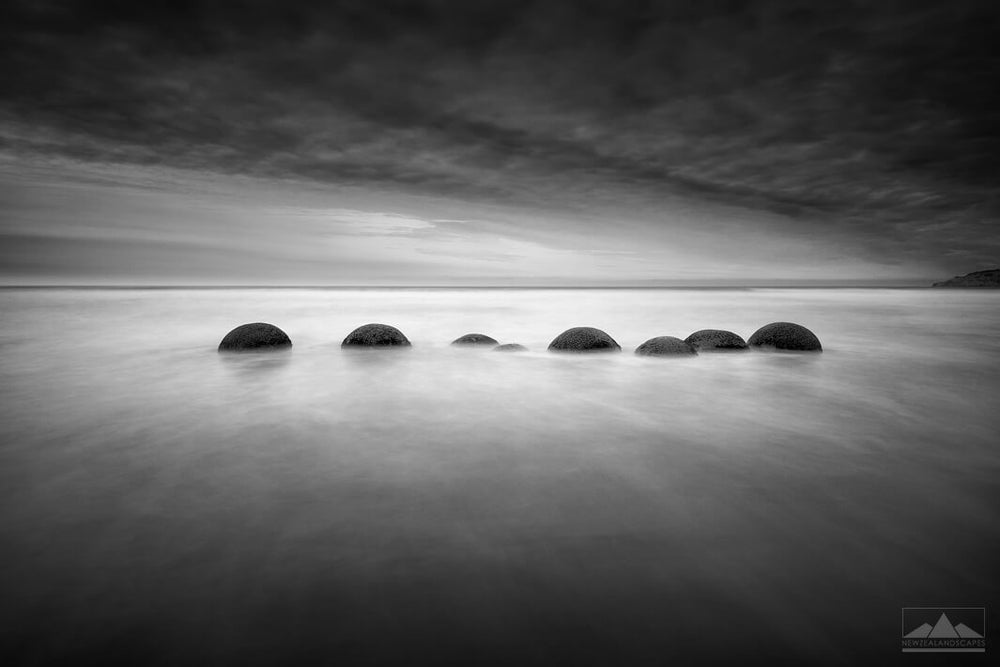 Black and white long exposure photo of eight Moeraki Boulders in a row.