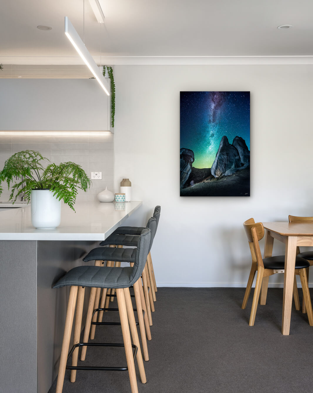 New Zealand landscape photo on canvas in modern kitchen with white bench, barstools, fern and dining setting