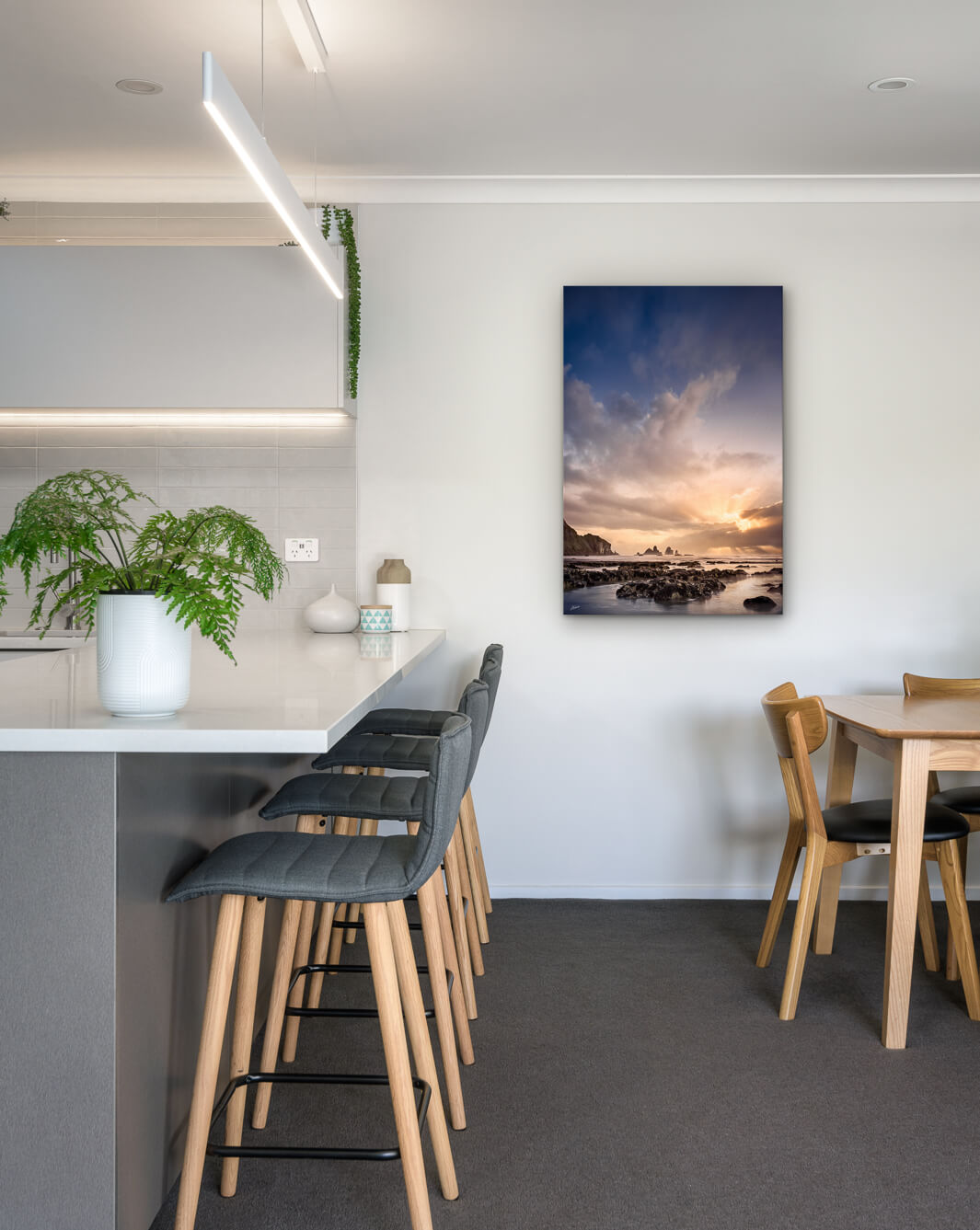New Zealand landscape photo on canvas in modern kitchen with white bench, barstools, fern and dining setting
