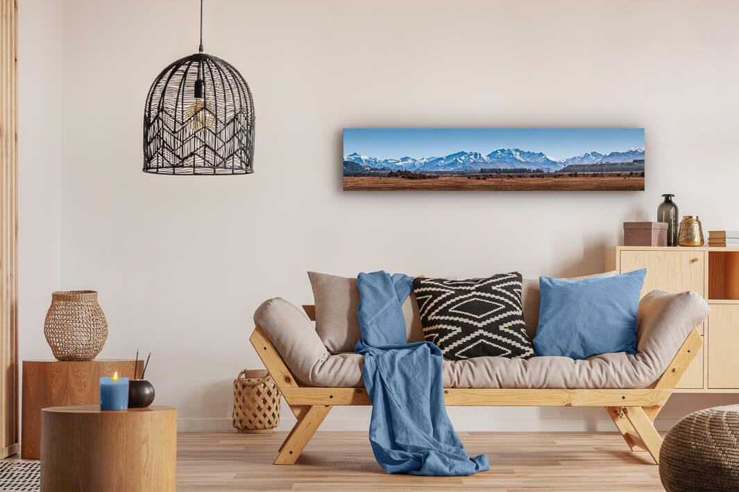 Canvas photo wall art of New Zealand landscape canvas print in lounge setting with a couch, cushions, coffee tables, and pendant light.