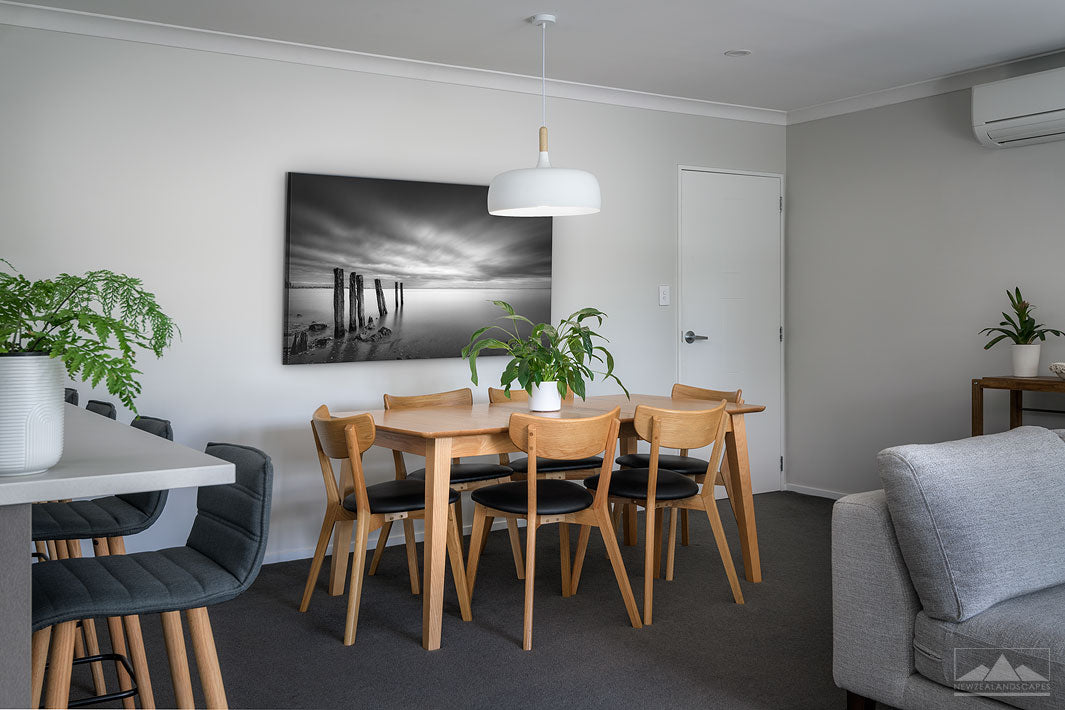 New Zealand landscape on canvas on a wall in a dining room with dining table & chairs, couch, coffee table & plants