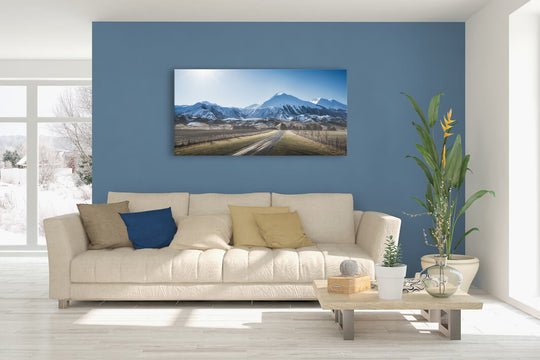 New Zealand landscape canvas photo wall art in lounge setting with a blue wall, white couch, coffee table, plant, cushions