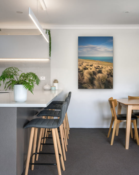 New Zealand landscape photo on canvas in modern kitchen with white bench, barstools, fern and dining setting