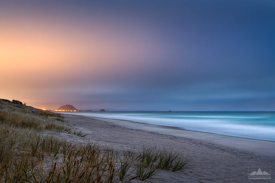 Evening view of Mount Maunganui from Papamoa Beach with city lights in the background and sand dunes in the foreground