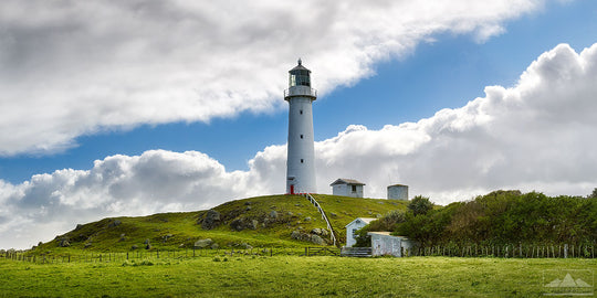 Panoramic photo of Cape Egmont lighthouse across the fields with large white clouds in the sky.