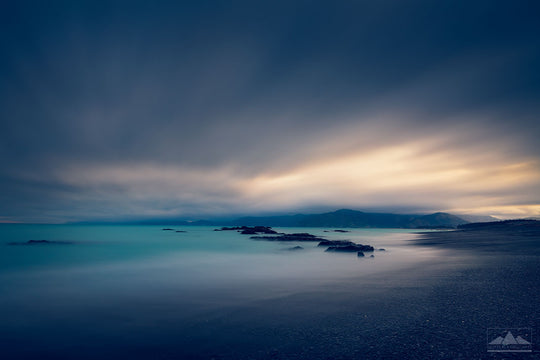 South Bay in Kaikoura at sunset with rocks in the foreground and pink orange sky