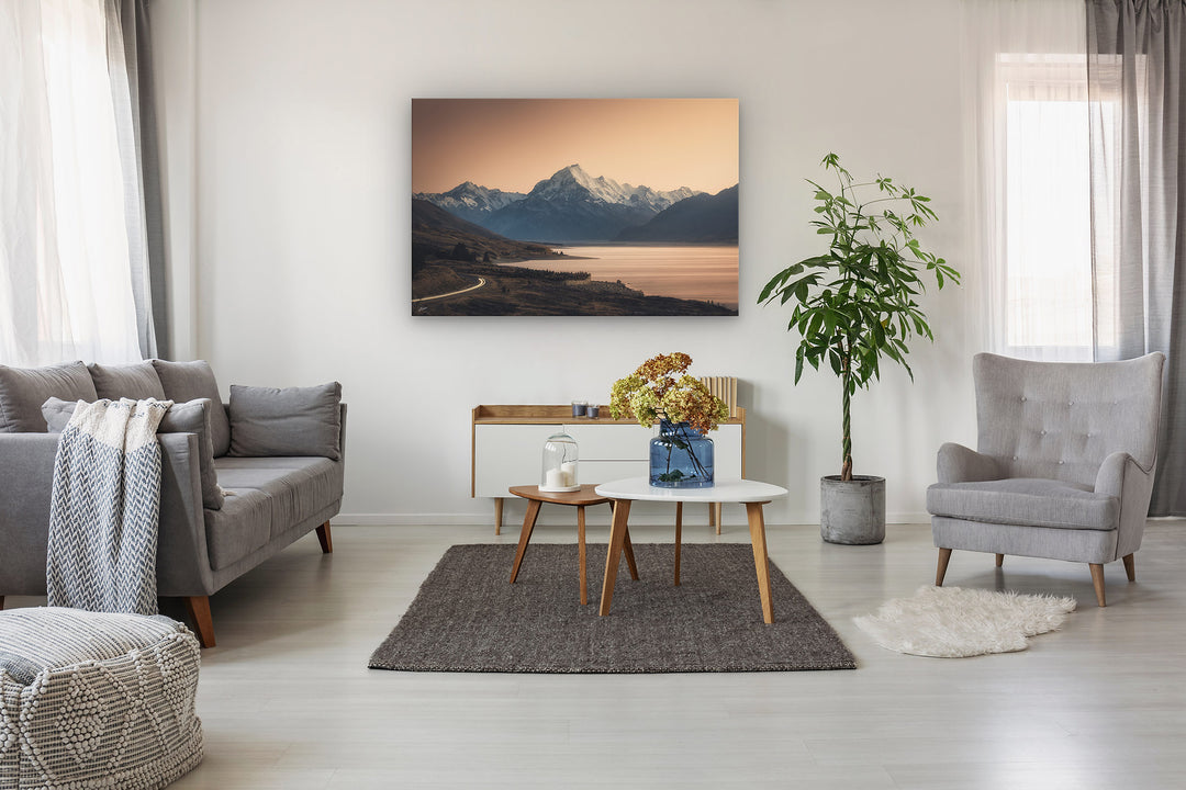 Mountain photo wall art in neutral lounge setting with a couch, rug, plant, flowers, chair and curtains