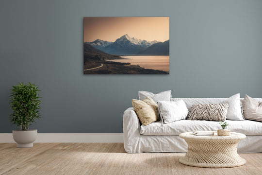 Mountain photo wall art in lounge setting with a grey wall, white couch, coffee table, plant, cushions