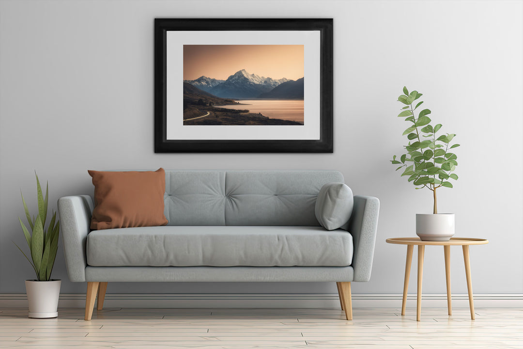 Framed wall art of mountains with a grey couch, plants and table.
