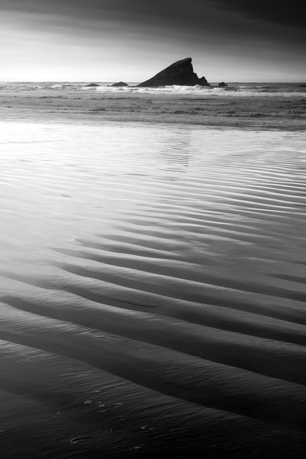 Rippled sand leading to the waves in the sea with a rock in the water.
