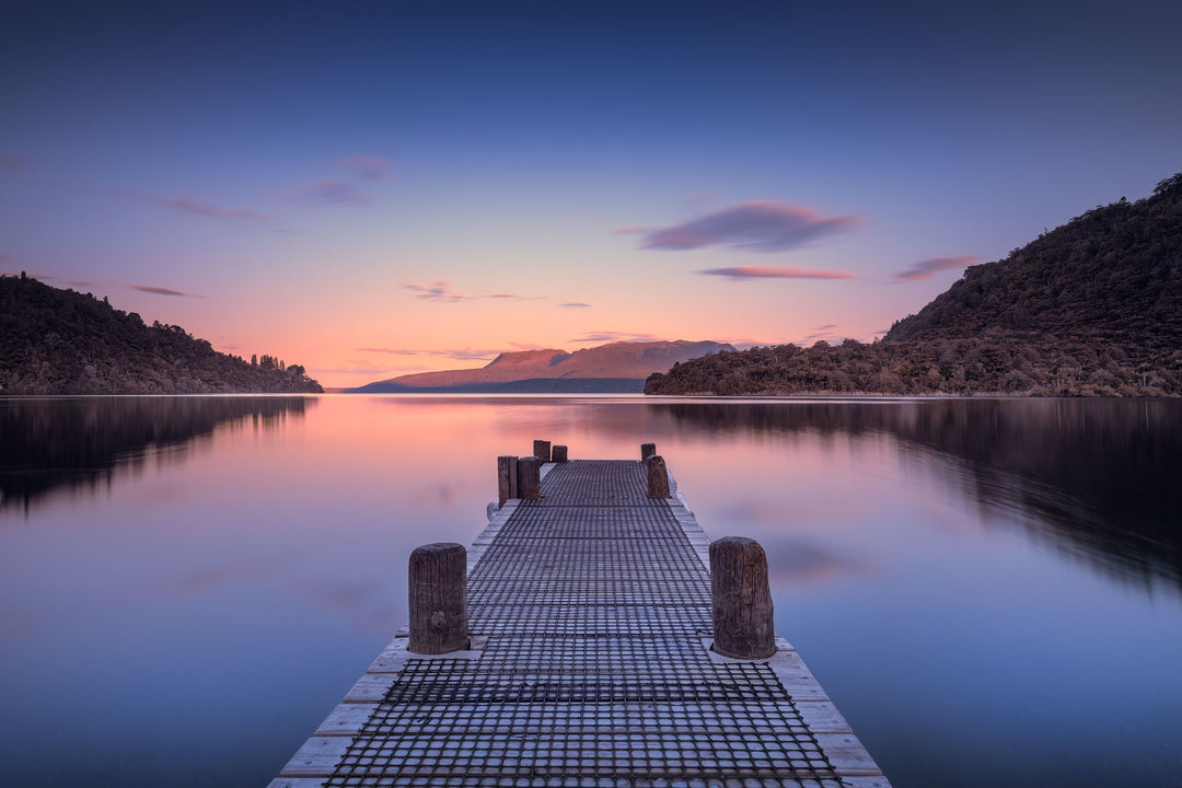 Evening sunset photo of a jetty at Lake Tarawera with still lake water and mountains and hills in the background