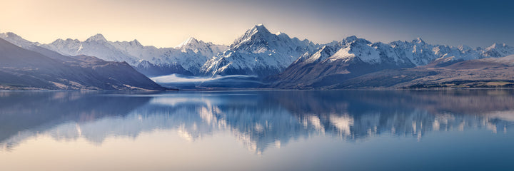 Panoramic landscape photo of snow covered mountains and Aoraki Mt Cook, reflected in the still water of Lake Pukaki.