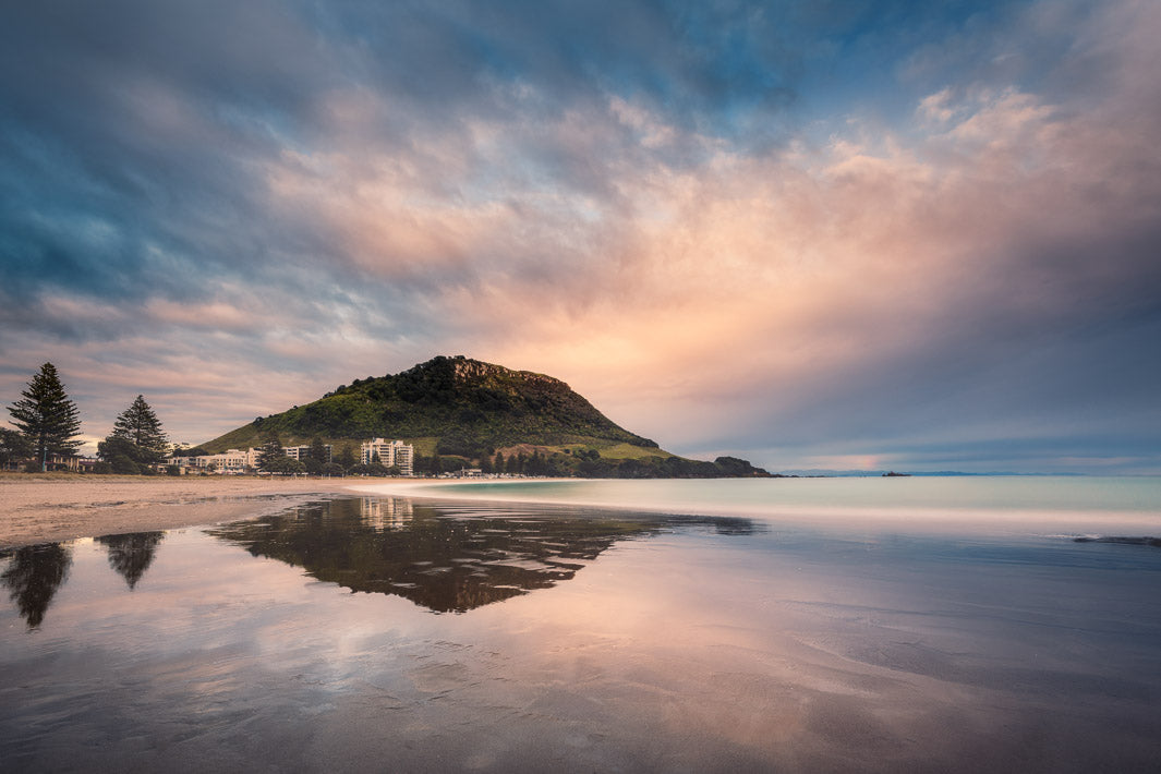 Long exposure early morning sunrise photo of Mount Maunganui reflected in the shallow waters and sand
