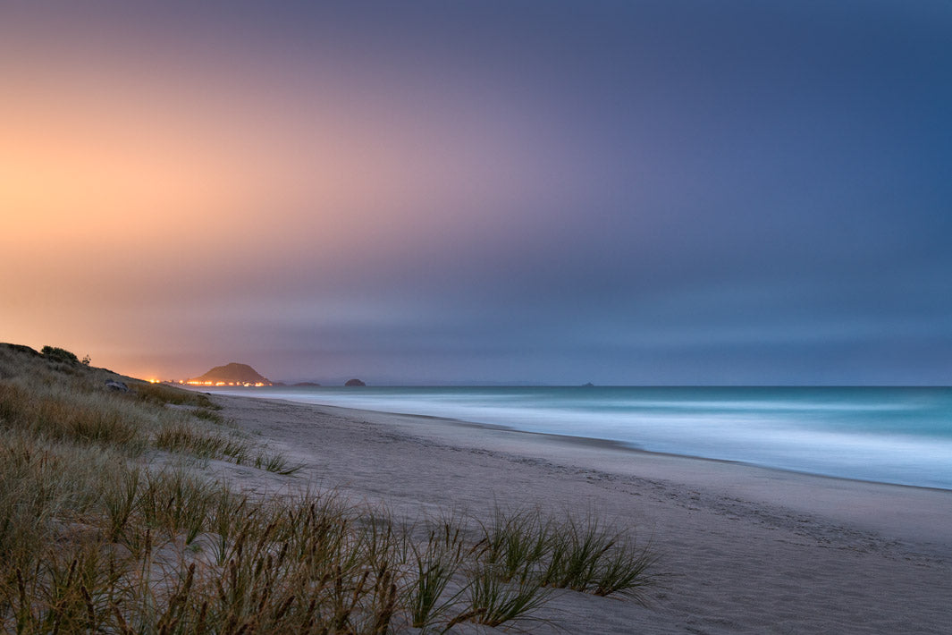 Evening view of Mount Maunganui from Papamoa Beach with city lights in the background and sand dunes in the foreground