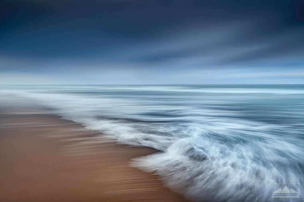 abstract beach photo of golden sand, blue sky, and the movement of the waves blurred in camera.