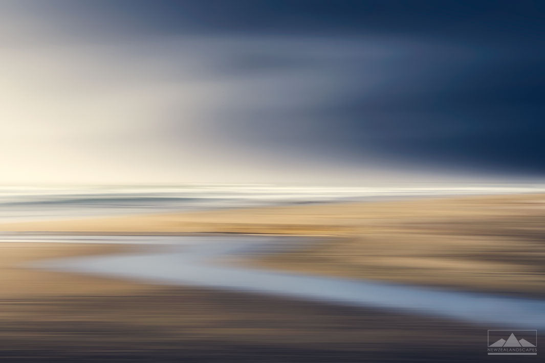 Abstract blurred photo of a stream leading to the beach, with golden sands and dark blue sky