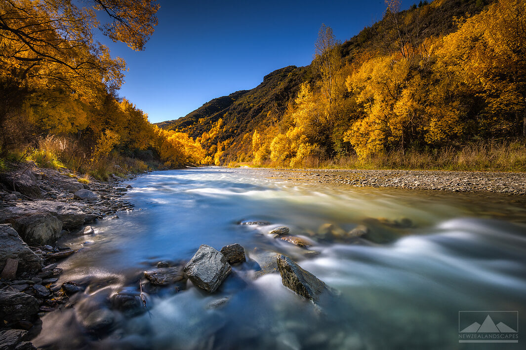 A long exposure photo of the Arrow River and golden autumn leaves of the trees in Arrowtown, Otago.