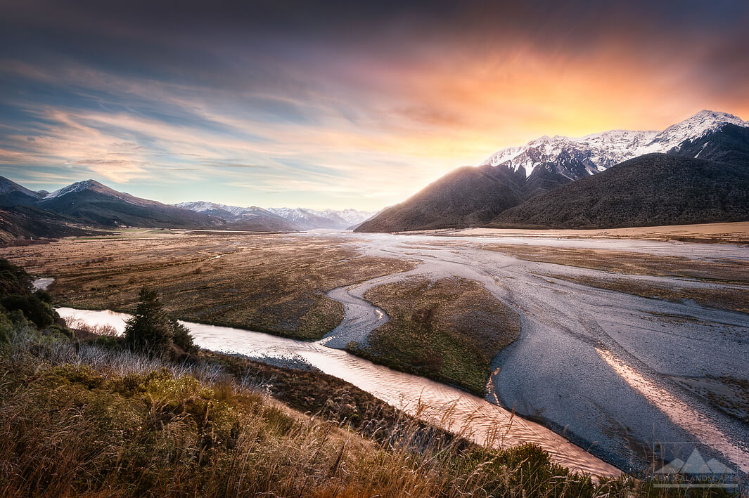 The setting sun behind the snowy mountains and river at Arthurs Pass by the Great Alpine Highway.
