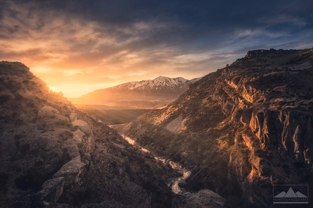 Landscape photo of mountains and a stream, with the sunrise lighting up the mountains