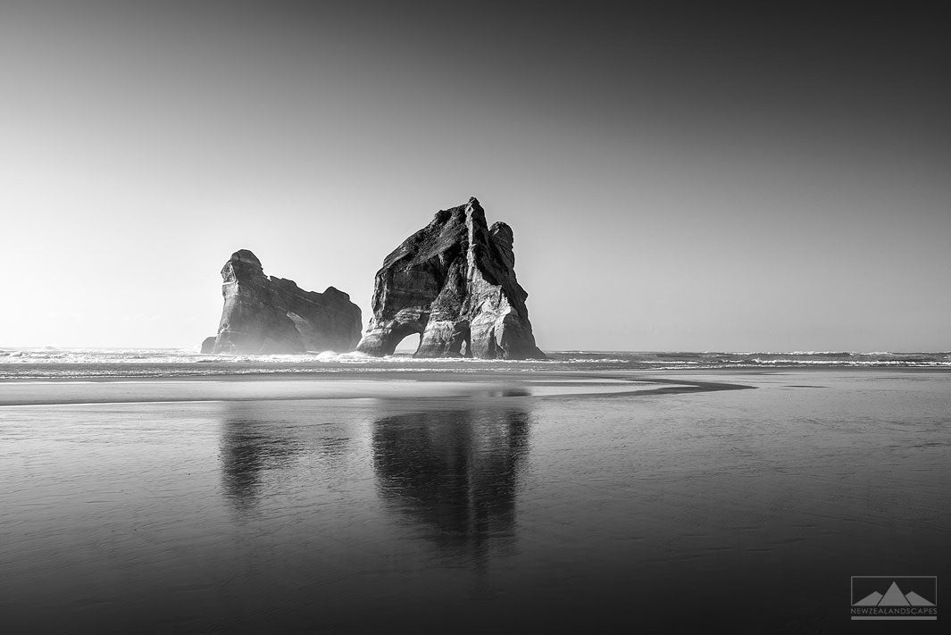 Black and white photo of huge rocks called Archway Islands, in the sea at Wharariki Beach in Tasman, New Zealand