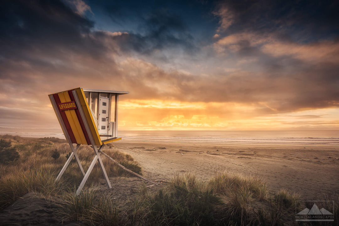 red and yellow lifeguard tower on Woodend Beach with the rising sun illuminating the clouds above.