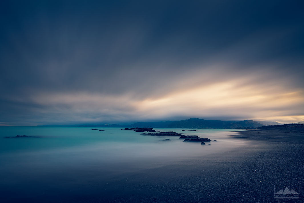 South Bay in Kaikoura at sunset with rocks in the foreground and pink orange sky