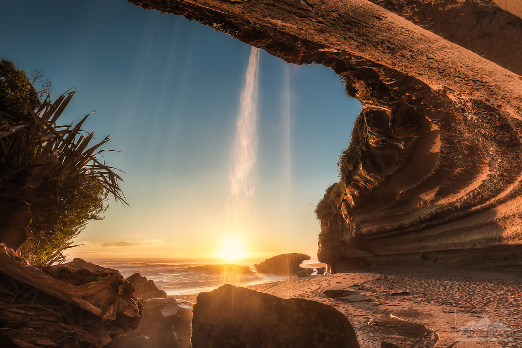 sunset at sea, viewed from a cave with small waterfall trickling down in front