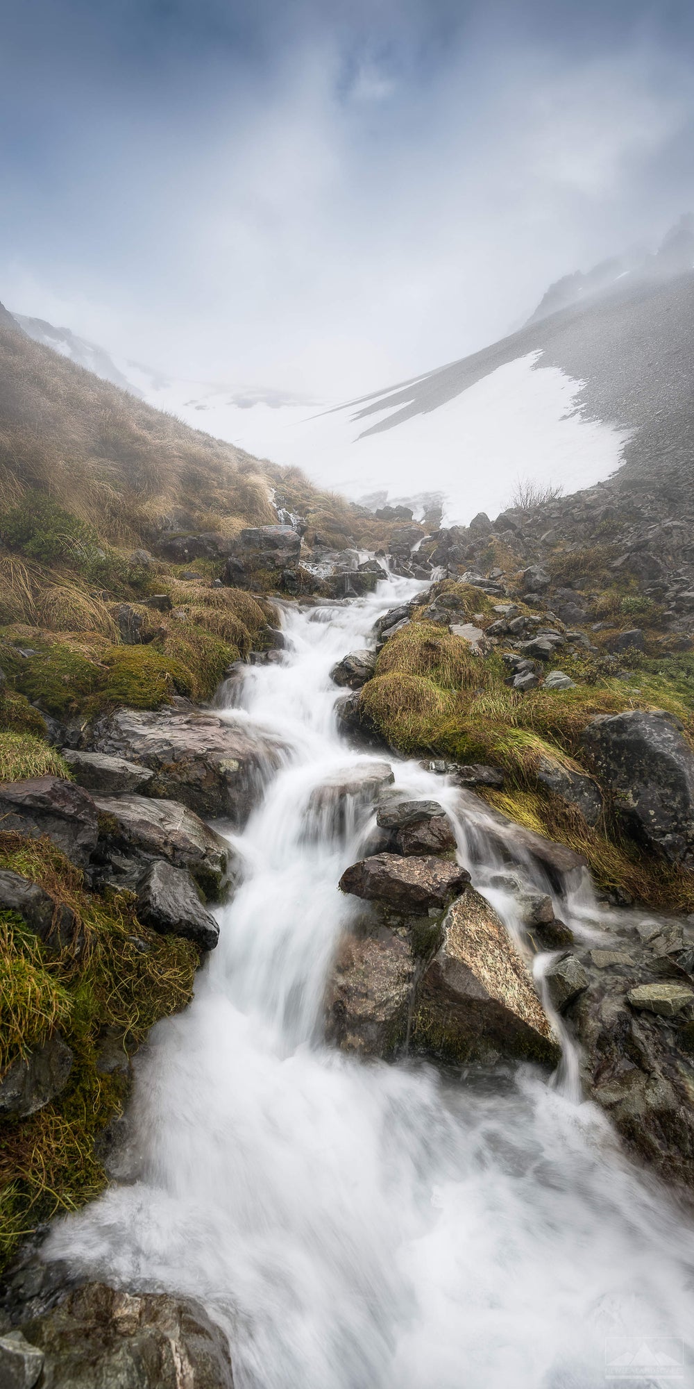 vertical photograph of a snowy mountain with a waterfall running down rocks in the centre of the image