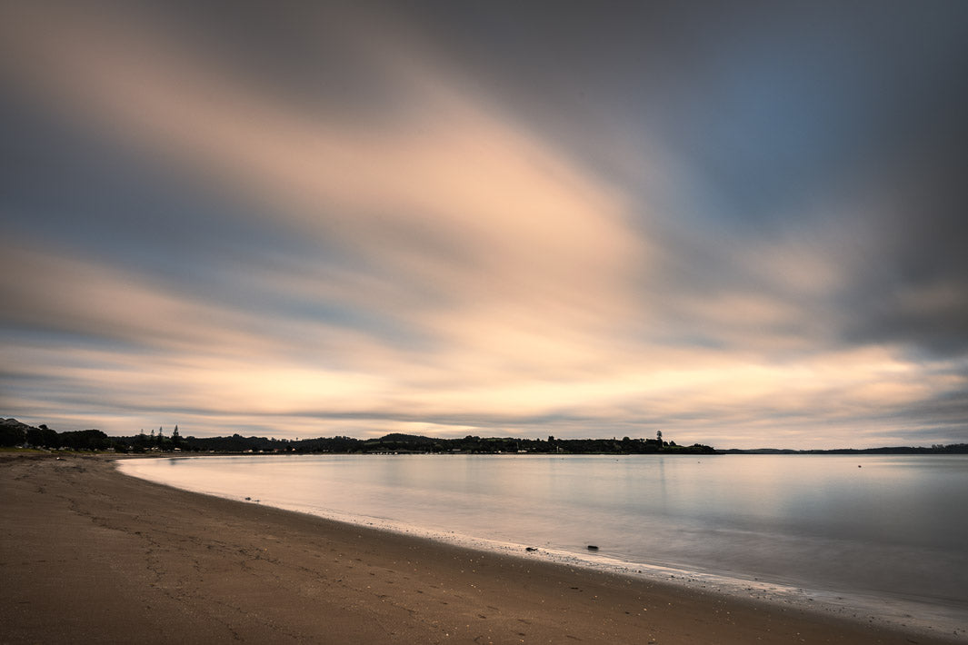 Sandy bay with pink evening sunset sky and long exposure smooth sea water.