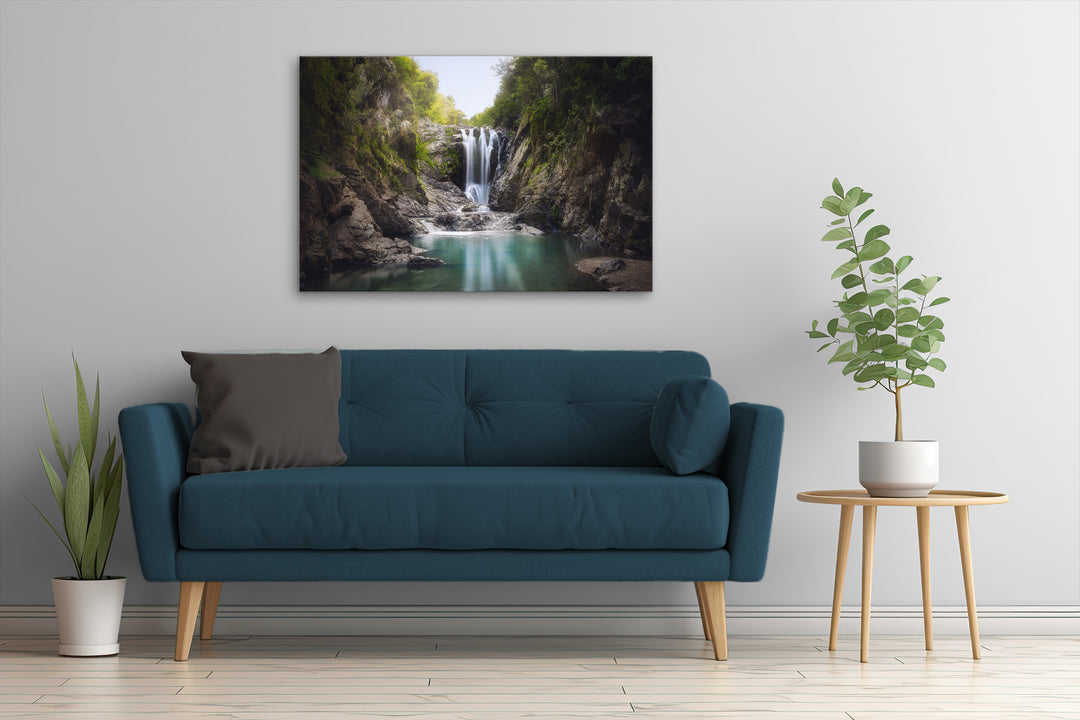 Piroa Falls wall art on a white wall above a dark couch, highlighting the waterfall and lush green forest in a modern living room setting.