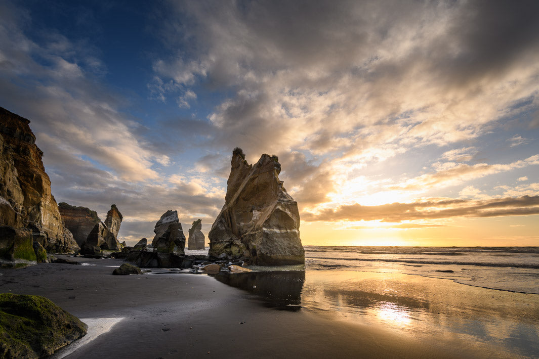 NZ landscape photo of the Three Sisters in Tongaporutu with rocks, sea and the sun setting behind the horizon