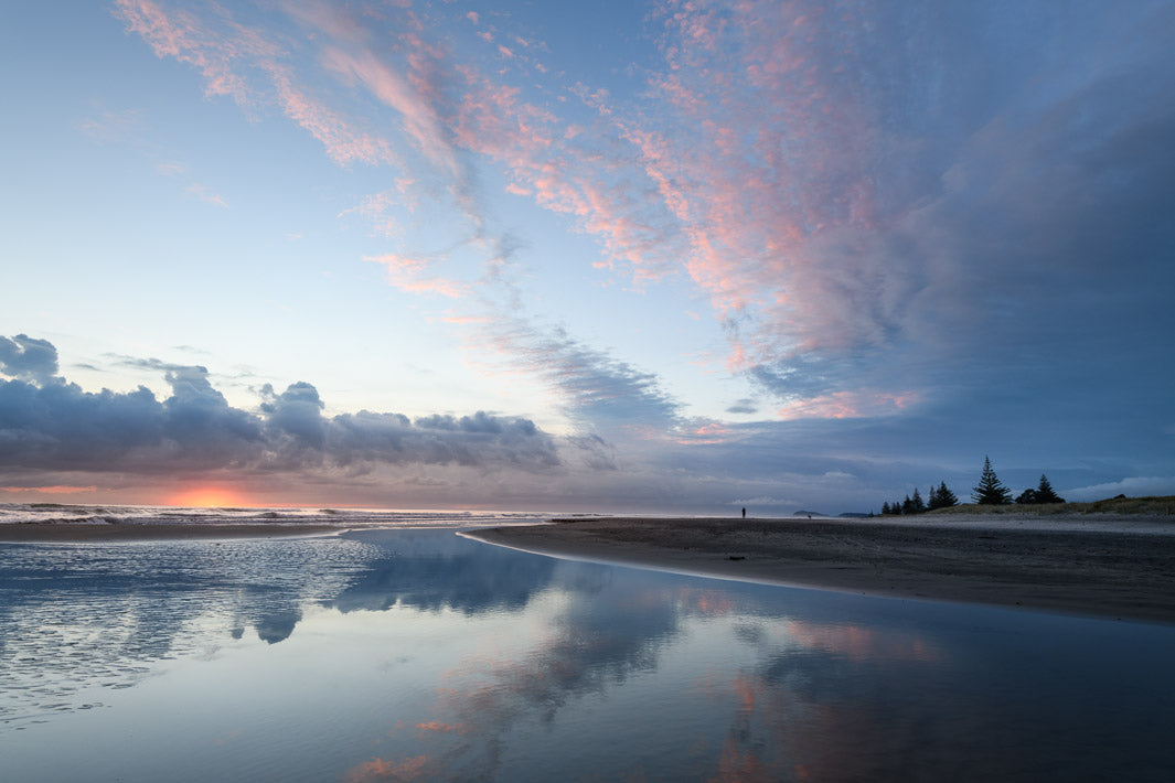 Reflection of the clouds in the sea with the sand and trees to the right.