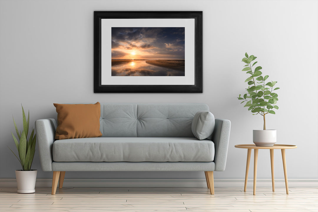 Framed wall art of New Zealand beach with a grey couch, plants and table.