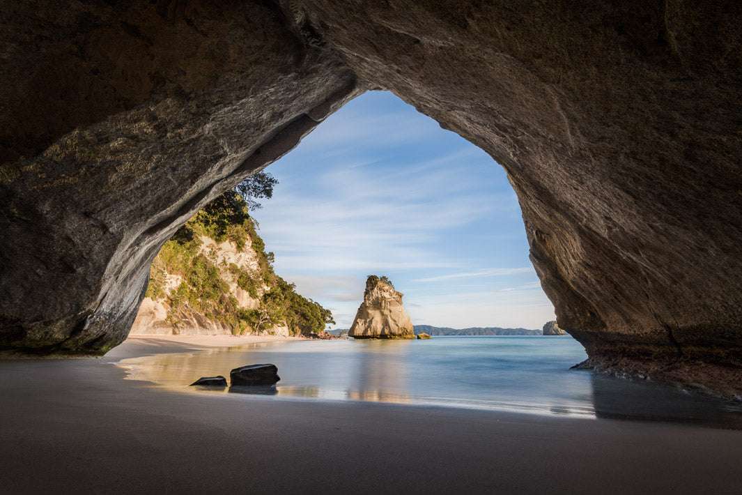 Looking through a cove to a rock in the sea that's reflected in the sand.