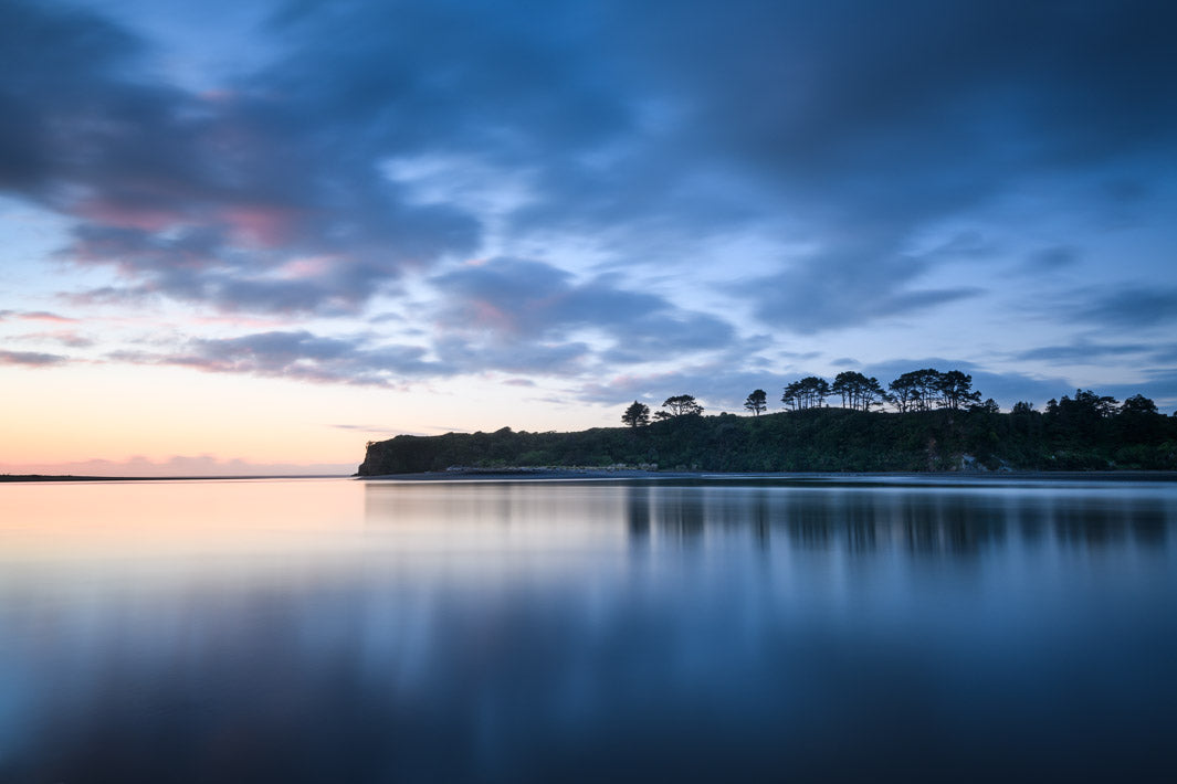 Photo of New Zealand scene of Tongaporutu River meeting the ocean with blue evening light in the water and the sky.