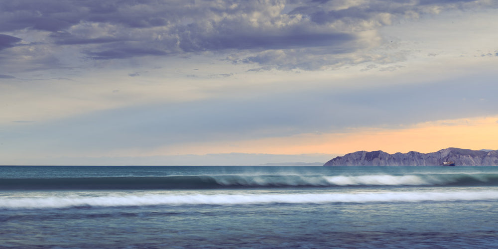 Photo of soft pastel colours of the waves at Waikanae Beach in Gisborne, at evening with the sun setting