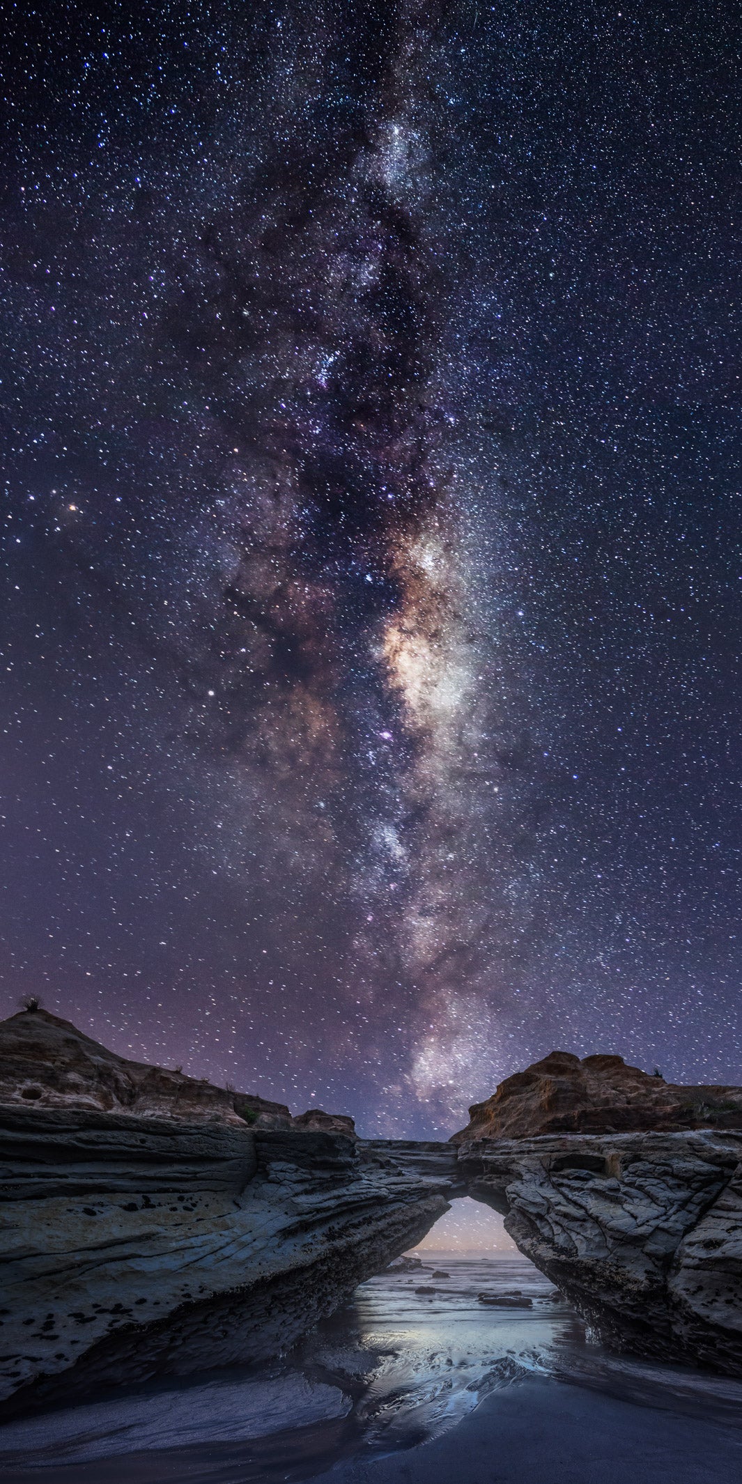 Milky Way astro photography in the night sky with rocks and sea below.