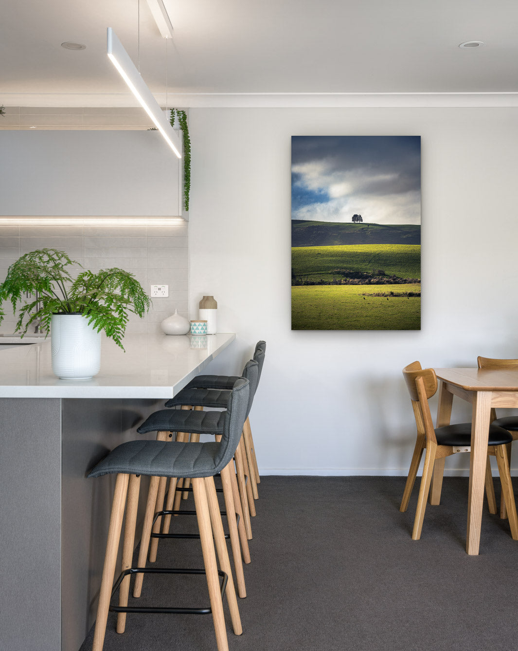 New Zealand landscape photo on canvas in modern kitchen with white bench, barstools, fern and dining setting