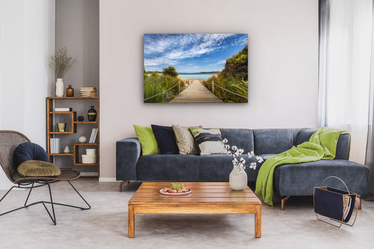 Large photo print wall art above a lounge suite with cushions, with a coffee table, chair and bookcase in the room.