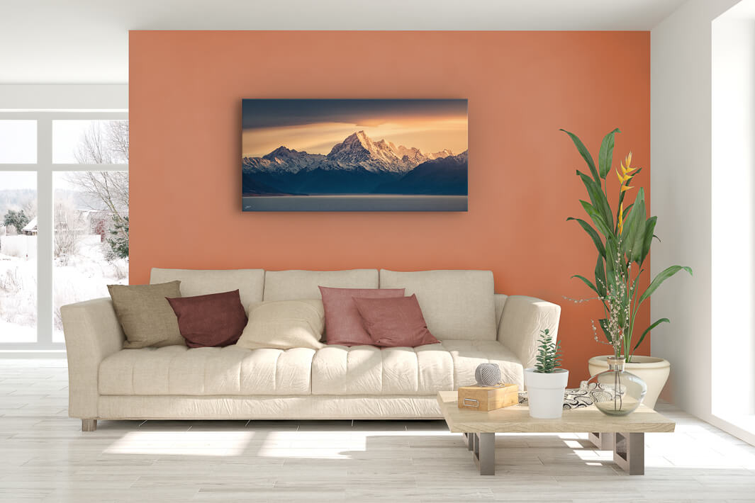 New Zealand landscape canvas photo wall art in lounge setting with a peach wall, white couch, coffee table, plant, cushions